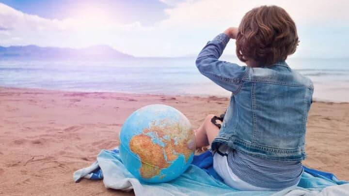 Une petite fille sur la plage regarde vers la mer avec un ballon symbolisant la terre à ses côtés